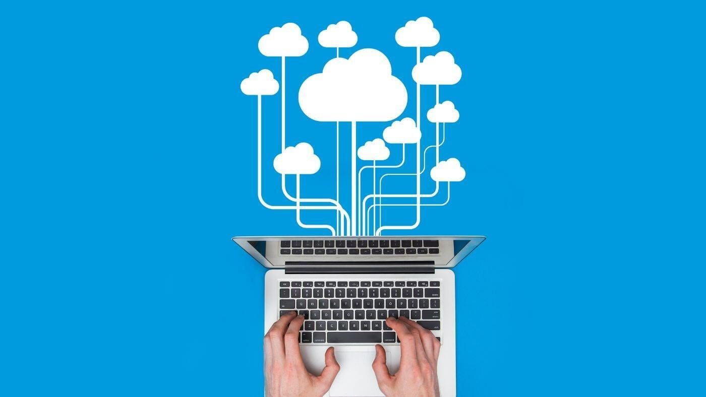 Hands typing on laptop aerial view with white clouds branching out over blue background